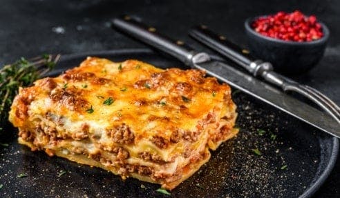 A portion of lasagne on a plate with cutlery