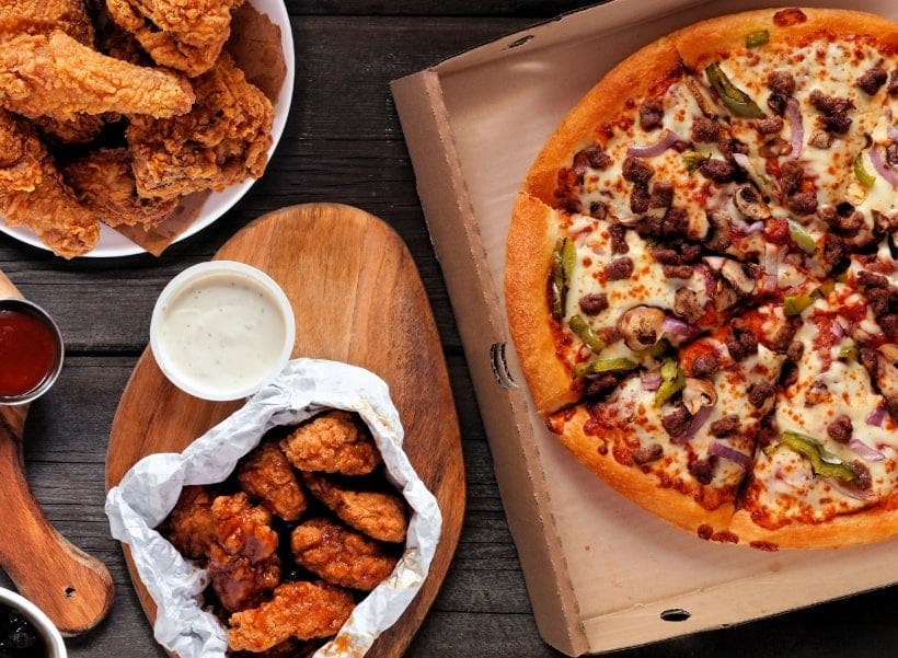 Pizza, fried chicken and wings with a dip served on a wooden table