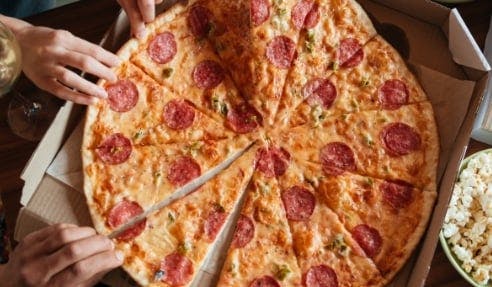 A pepperoni pizza being shared, with hands grabbing slices.