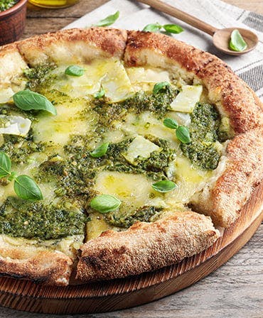 Pesto Pizza with Basil Leaves on Wooden Board